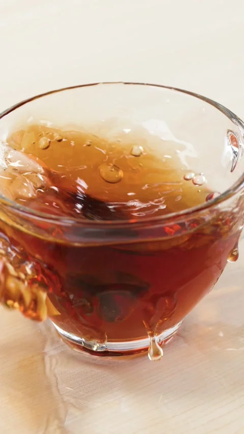 Tea Bag Dropping into Glass Cup with Splash on Wooden Table Stock Footage 345710750