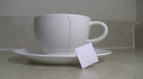 Tea bag dunked in white mug with saucer by hand on countertop Video stock 35533346