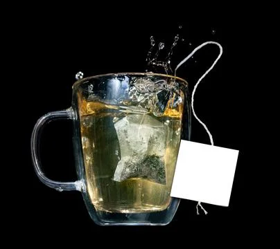A tea bag with empty label fall into a glass mug with hot water Stock Photos