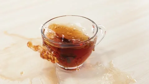 Tea Bag Falling into Glass Cup Causing Liquid Splash on Table Stock Footage 346121586