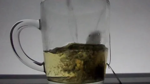 Tea bag in a glass cup being filled with hot water to make tea. Video stock 80023400