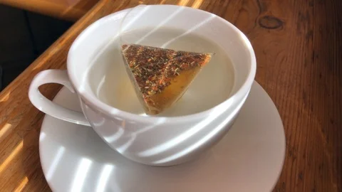 Tea bag with herbal tea being put into a cup of water Stock Footage 88082732