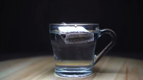 The tea bag is slowly dipped into the mug. Glare, black background. Video stock 169464735