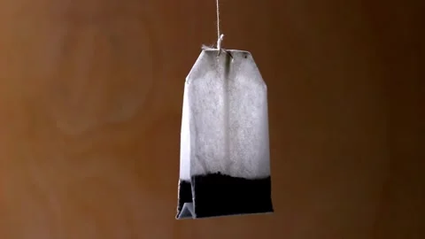 A tea bag is suspended from a string and slowly rotates against a backdrop light 库存影片 331832098