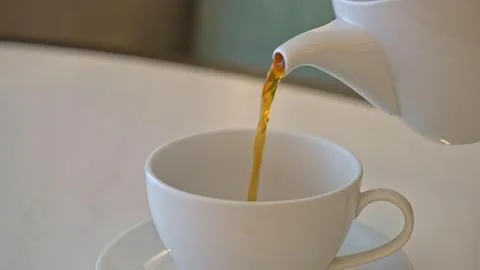 Tea being poured into a white ceramic cup from a teapot Stock Photos