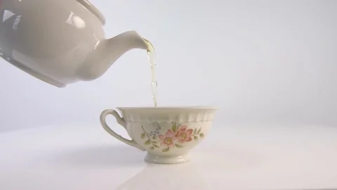 Tea being poured from a white teapot to a white floral teacup Stock Footage 85363126