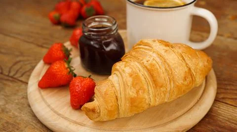 Tea break snacks. Lemon tea, croissant, jar of jam and fresh strawberries. Stock Photos