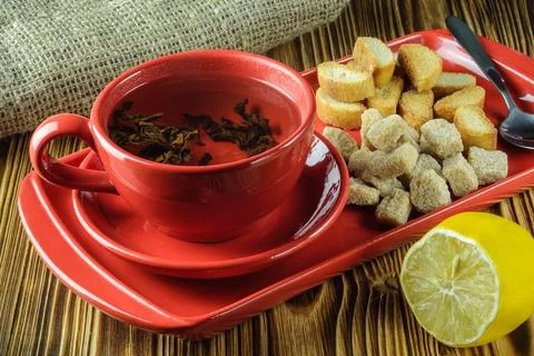 Tea break. Tea in a red ceramic cup on a tray with lump reed sugar, crackers Stock Photos