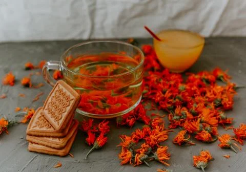 Tea with calendula flowers and biscuits. Transparent glass cup and saucer Stock Photos