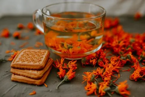 Tea with calendula flowers and biscuits. Transparent glass cup and saucer Stock Photos