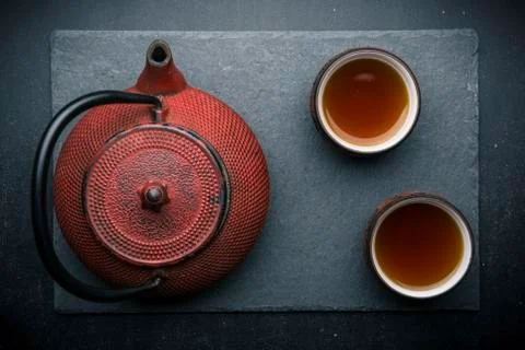 Tea composition with ceramic tea cups and red iron teapot on dark stone backg Stock Photos