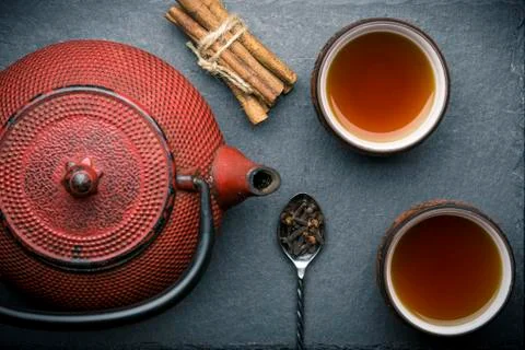 Tea composition with ceramic tea cups and red iron teapot on dark stone backg Stock Photos