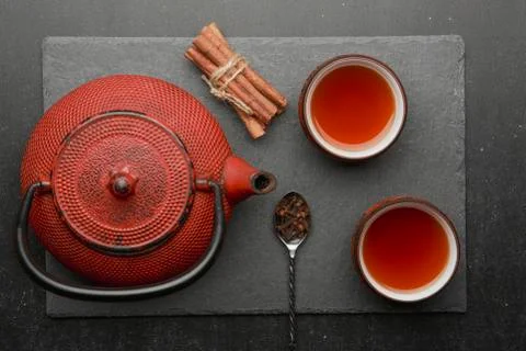 Tea composition with ceramic tea cups and red iron teapot on dark stone backg Stock Photos