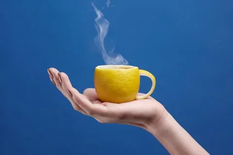 A tea cup made of lemon. Lemon cup in hand on a blue background. Creative c.. Stock Photos