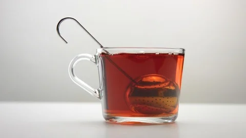 A tea infuser spoon moves in slow motion into a transparent tea cup Stock Footage 116717306