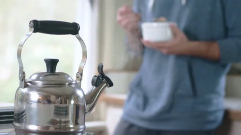 Tea kettle steaming on stove while young hispanic man eats cereal in background Stock Footage 84473111