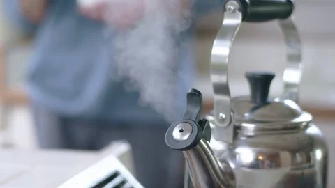 Tea kettle steaming on stove while young hispanic man eats cereal in background Stock Footage 84475760