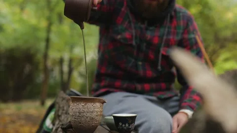 A tea master with a beard pours pu-erh tea from a clay teapot. outdoor tea Stock Footage 220415220