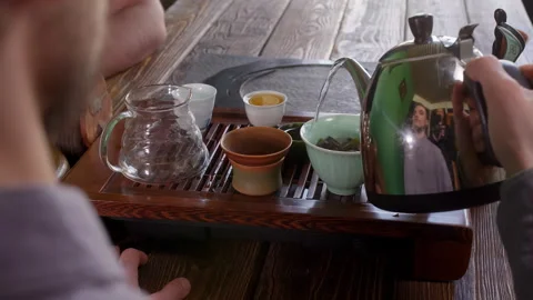 Tea master brewing large leaf tea in gaiwan pouring hot water from metal pot. Stock Footage 241012404