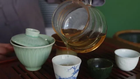 Tea master pouring fresh brewing tea to bowls on wooden table, hands close-up. Stock Footage 239050639