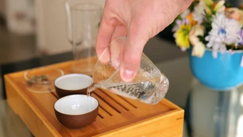 A tea master pours boiling water into clay bowls from a glass cup for washing Stock Footage 220341788