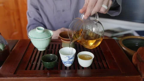 Tea master pours green oolong tea from fairness pitcher to tea bowls, close-up. Stock Footage 241012913