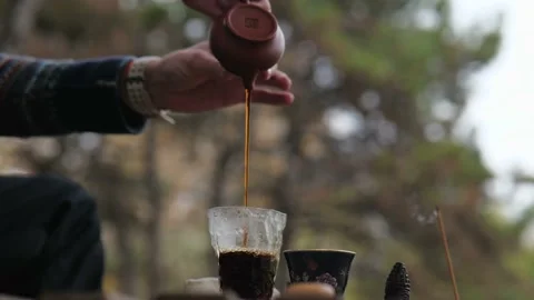 Tea master pours strong brewed pu-erh tea from a clay teapot into a glass Stock Footage 229860933