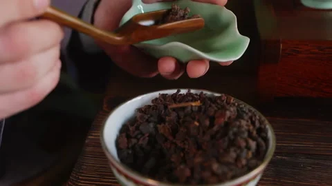 Tea master puts dry Cha he tea leaves from bowl to tea pitcher, hands close-up. Stock Footage 239050689