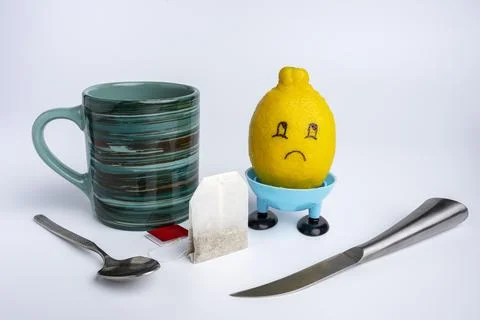 A tea mug with a tea bag, a sad lemon and a lemon knife 库存照片