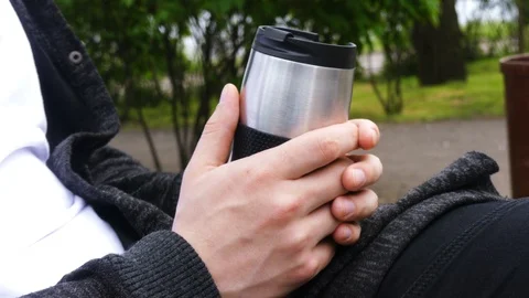 Tea or coffee time outdoors. Young man holding thermo cup / mug / jar tea or  Stock Footage 107901659