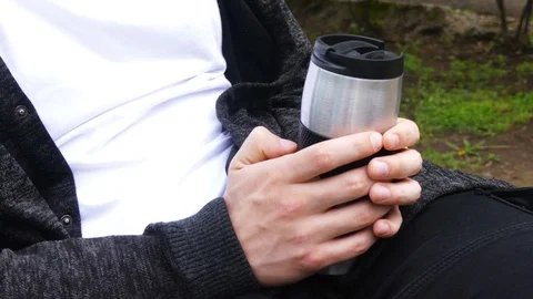 Tea or coffee time outdoors. Young man holding thermo cup / mug / jar tea or  Stock Footage 107901685