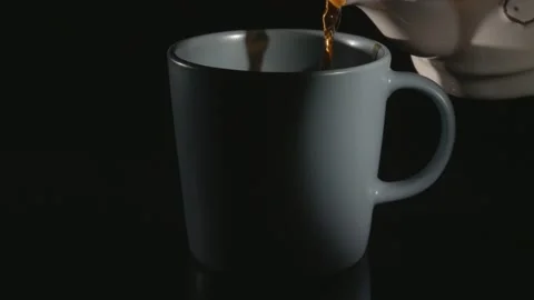 Tea is poured into a ceramic cup. Close-up against a black background. Stockbeeldmateriaal 147098035