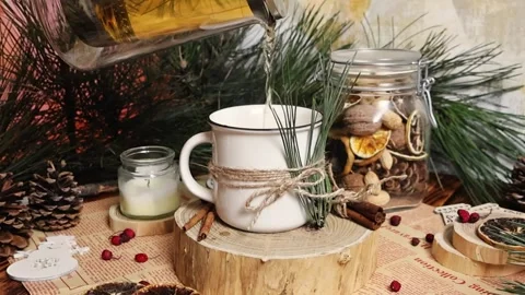Tea is poured from the transparent teapot into the mug decorated with a pine Stock Footage 292969887