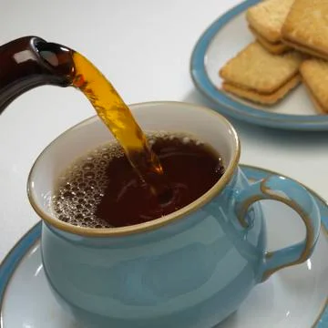 TEA POURING INTO CUP WITH BISCUITS IN BACKGROUND Stock Photos