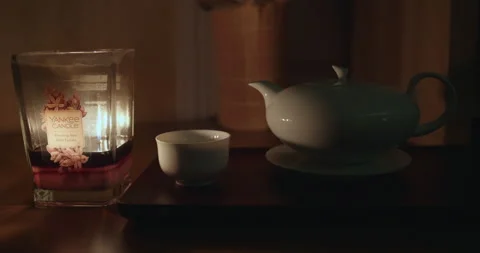 Tea set next to a burning Yankee candle for a peaceful night Stock Footage 153170386
