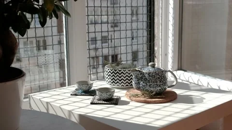Tea set next to a window and a potted plant on a sunny afternoon. Staycation. Video stock 140460293