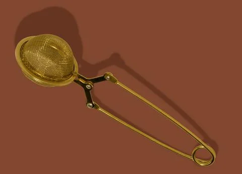 Tea strainer isolated on brown background. Gold metal tea infuser. Stock Photos