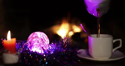 Tea from a teapot pours into a cup standing on the table next to a candle . 스톡 동영상 221913144