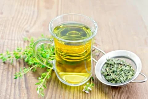 Tea of thyme in mug with strainer on old board Stock Photos