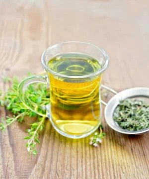 Tea of thyme in mug with strainer on old wooden board Stock Photos