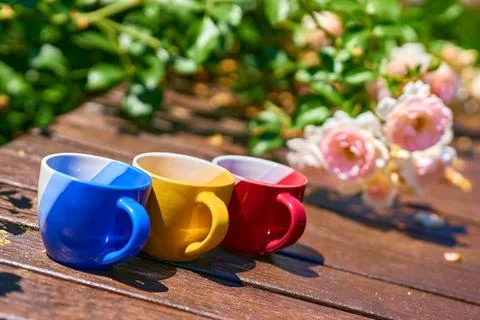 Tea time. Coffee break. Blue red yellow cups on wooden in blooming garden Stock Photos