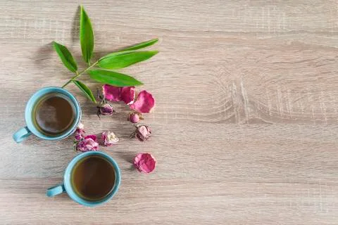 Tea time composition. Two cups of tea, red rose buds and green bamboo leaves  Stock Photos