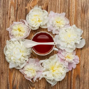 Tea time. Flat lay over wooden background with peonies, cup of tea and spoon Stock Photos