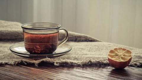 Tea in a transparent glass cup and dried lemon on the edge of a rough burlap Stock Photos