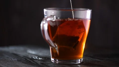 Tea in transparent glass cup rotated over black wooden background Stock Footage 101895448