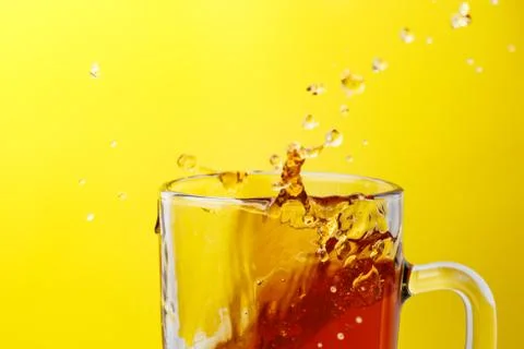 Tea in transparent mug on a yellow background splashed wiht ice Stock Photos