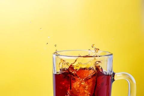 Tea in transparent mug on a yellow background splashed wiht ice Stock Photos