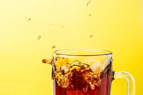 Tea in transparent mug on a yellow background splashed wiht ice Stock Photos