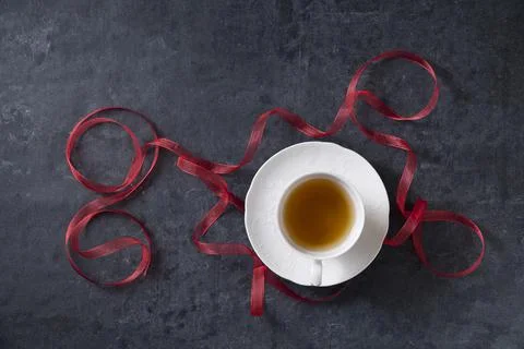 Tea in white ceramic cup on a dark background with a red ribbon christmas party Stock Photos