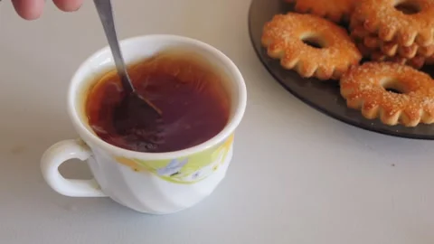 Tea in a white cup on a table with sweets is stirred with a spoon. Medium sho Stock Footage 318981165